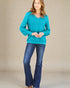 Woman wearing a teal sweater and blue jeans against a beige background