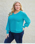 Woman wearing a turquoise sweater and blue pants against a textured beige wall.