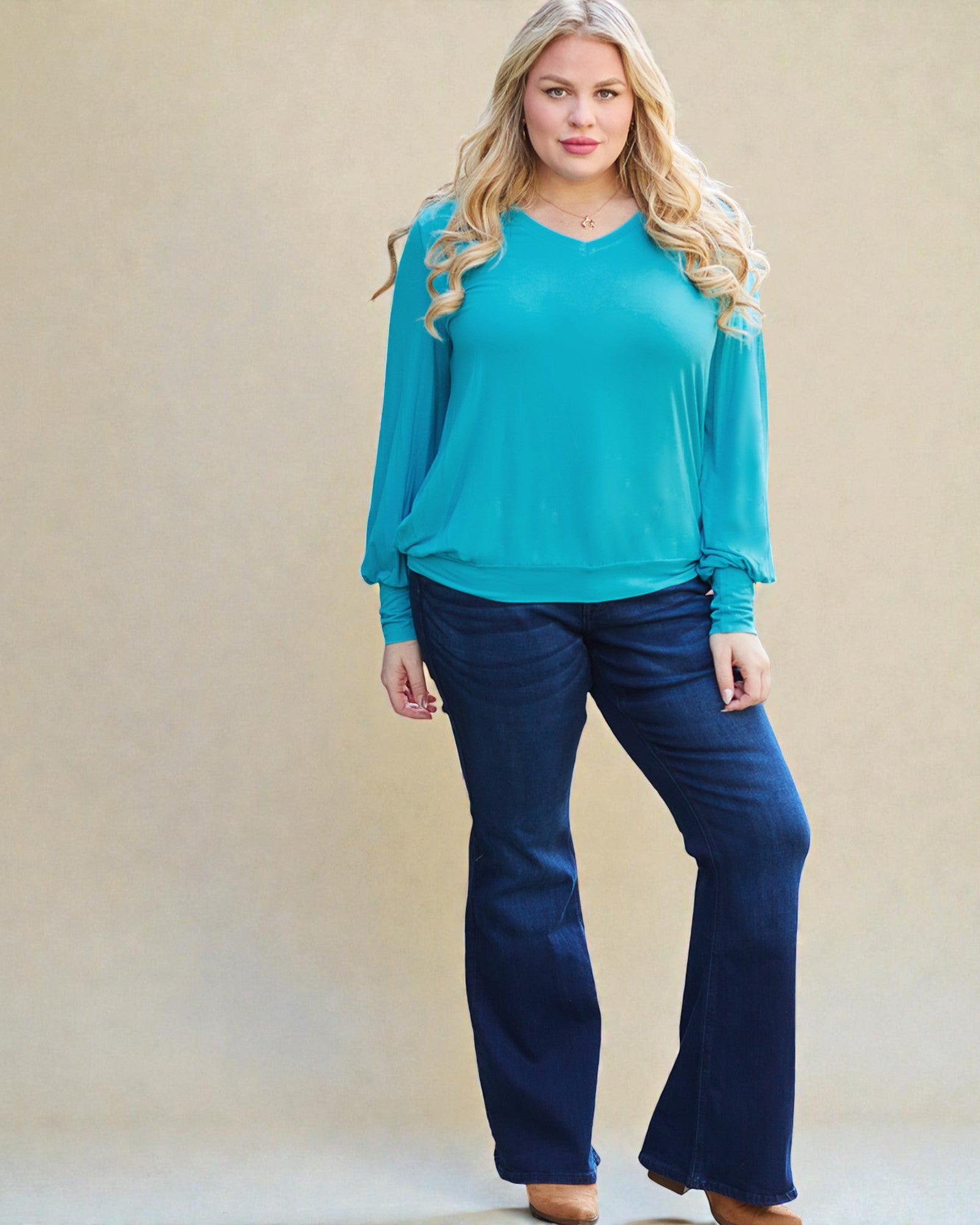 Woman wearing a turquoise top and blue jeans against a beige background