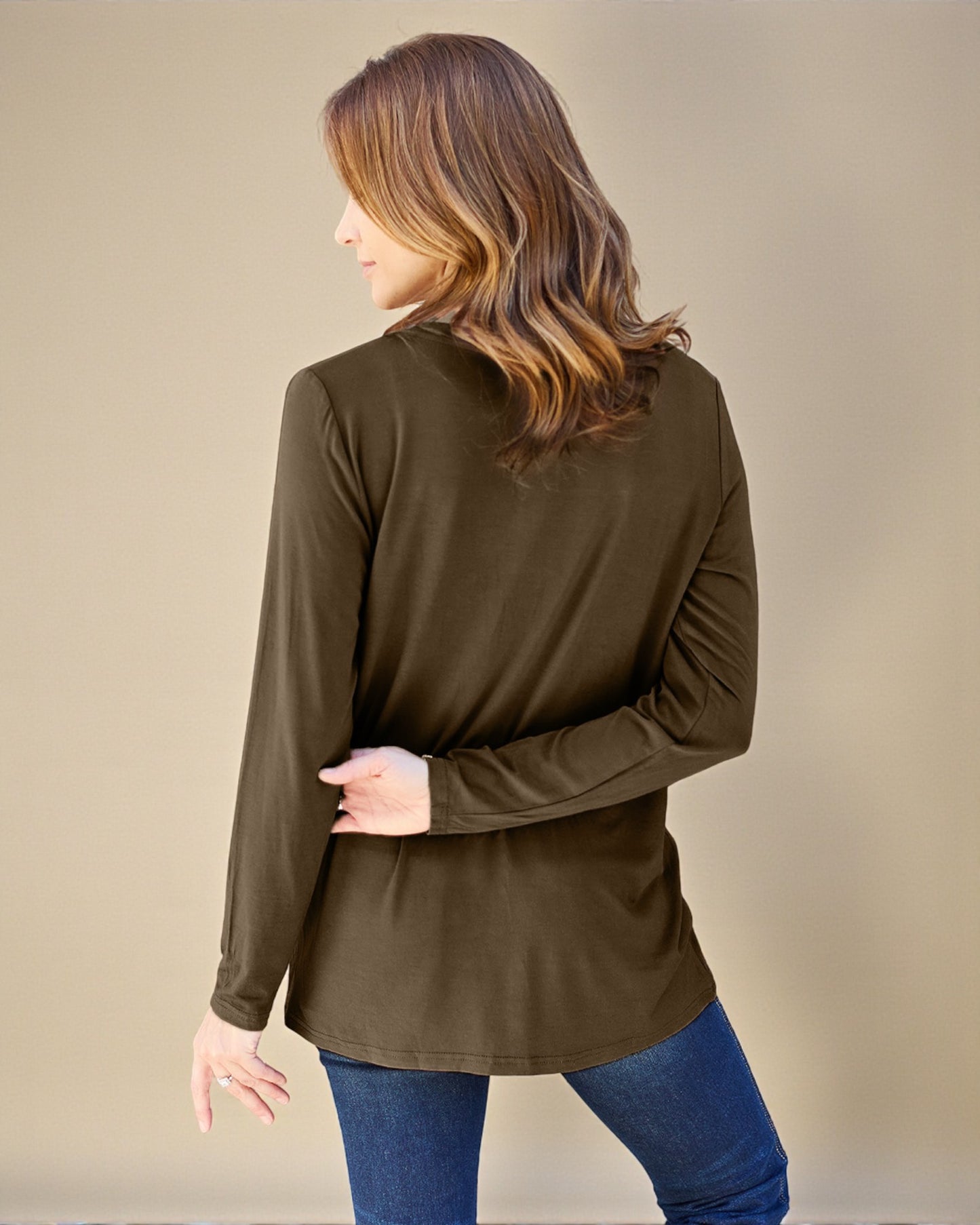 Woman wearing a brown long-sleeve top and blue jeans against a beige background