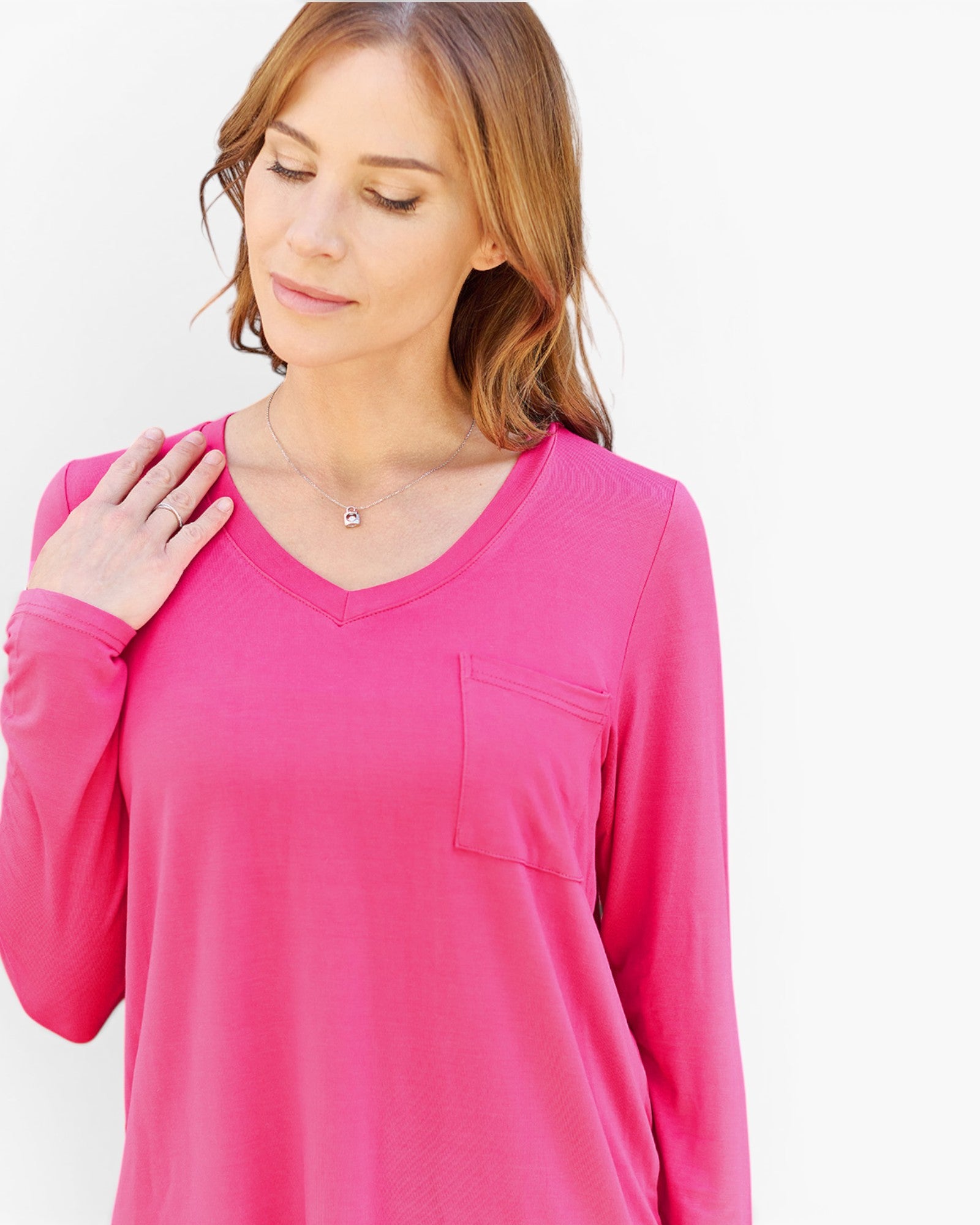 A woman wearing a bright pink long-sleeve V-neck top with a chest pocket, shown against a plain light background.