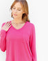 A woman wearing a bright pink long-sleeve V-neck top with a chest pocket, shown against a plain light background.