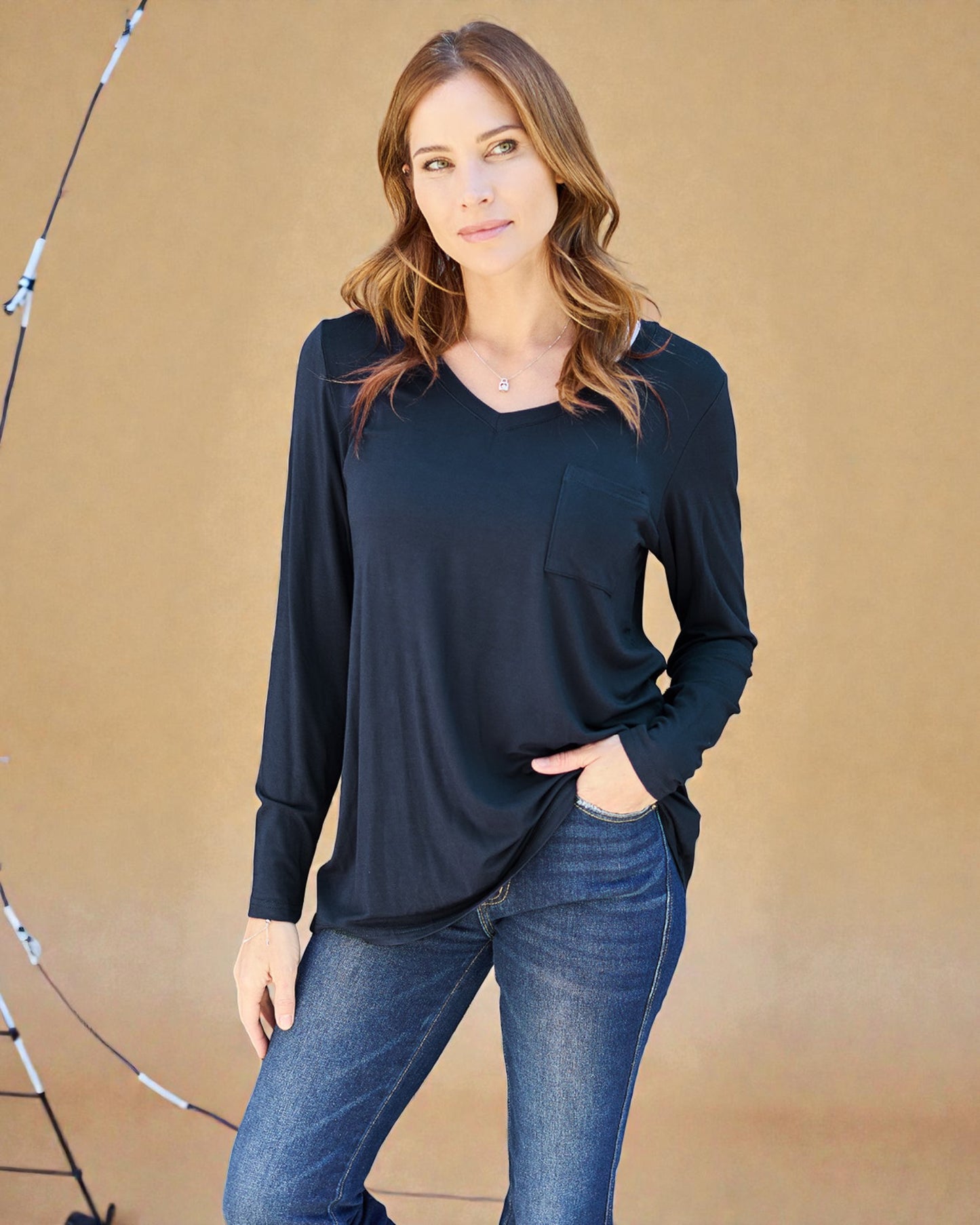 Woman wearing a black long-sleeve top and blue jeans against a beige background