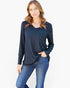 A woman modeling a dark navy blue long-sleeve top with a split neckline and a chest pocket, paired with blue jeans, against a plain white background.