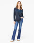 A woman modeling a dark navy blue long-sleeve top with a split neckline, paired with blue jeans and white platform shoes, against a plain white background.