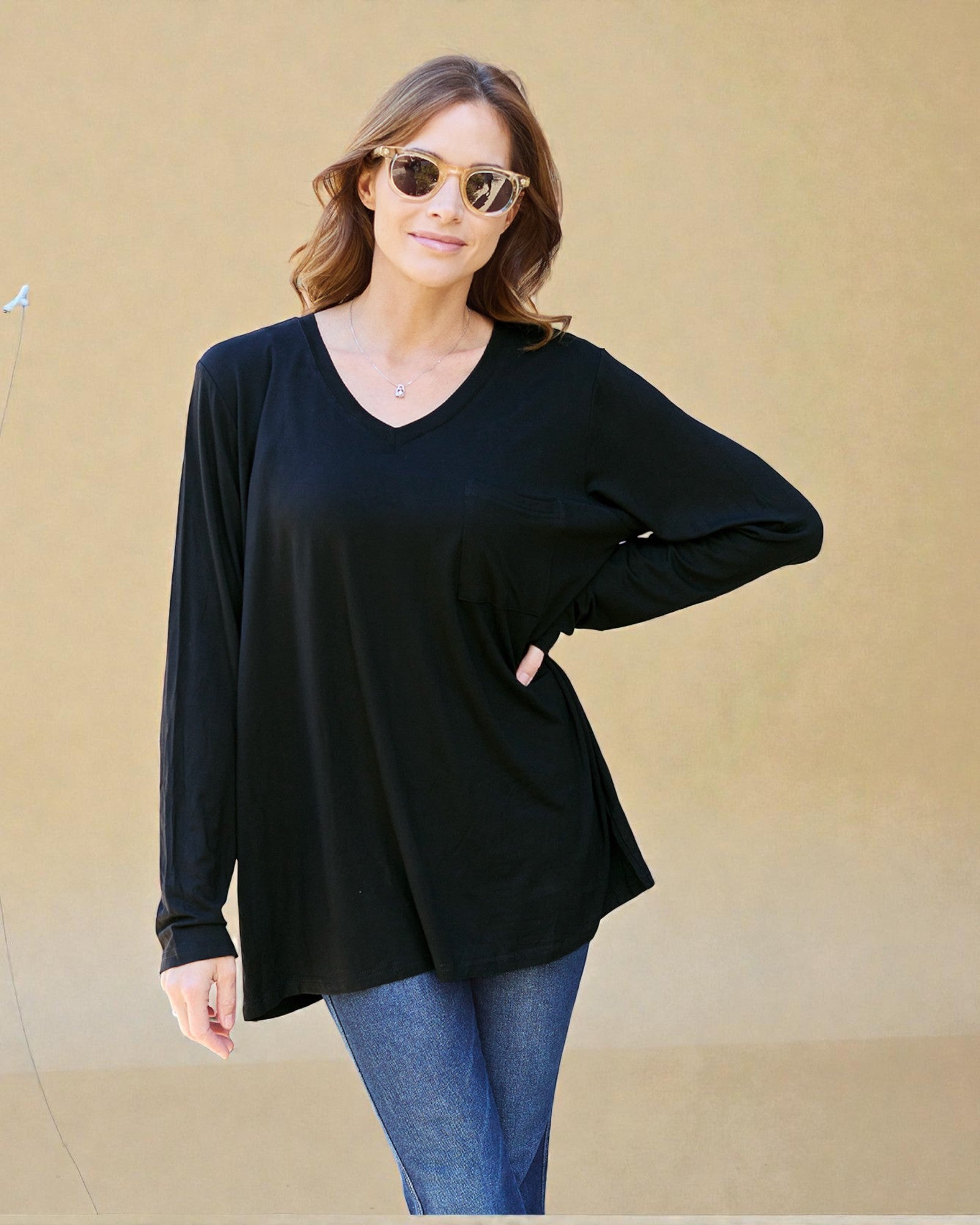 Woman wearing a black long-sleeve top and blue jeans against a beige background