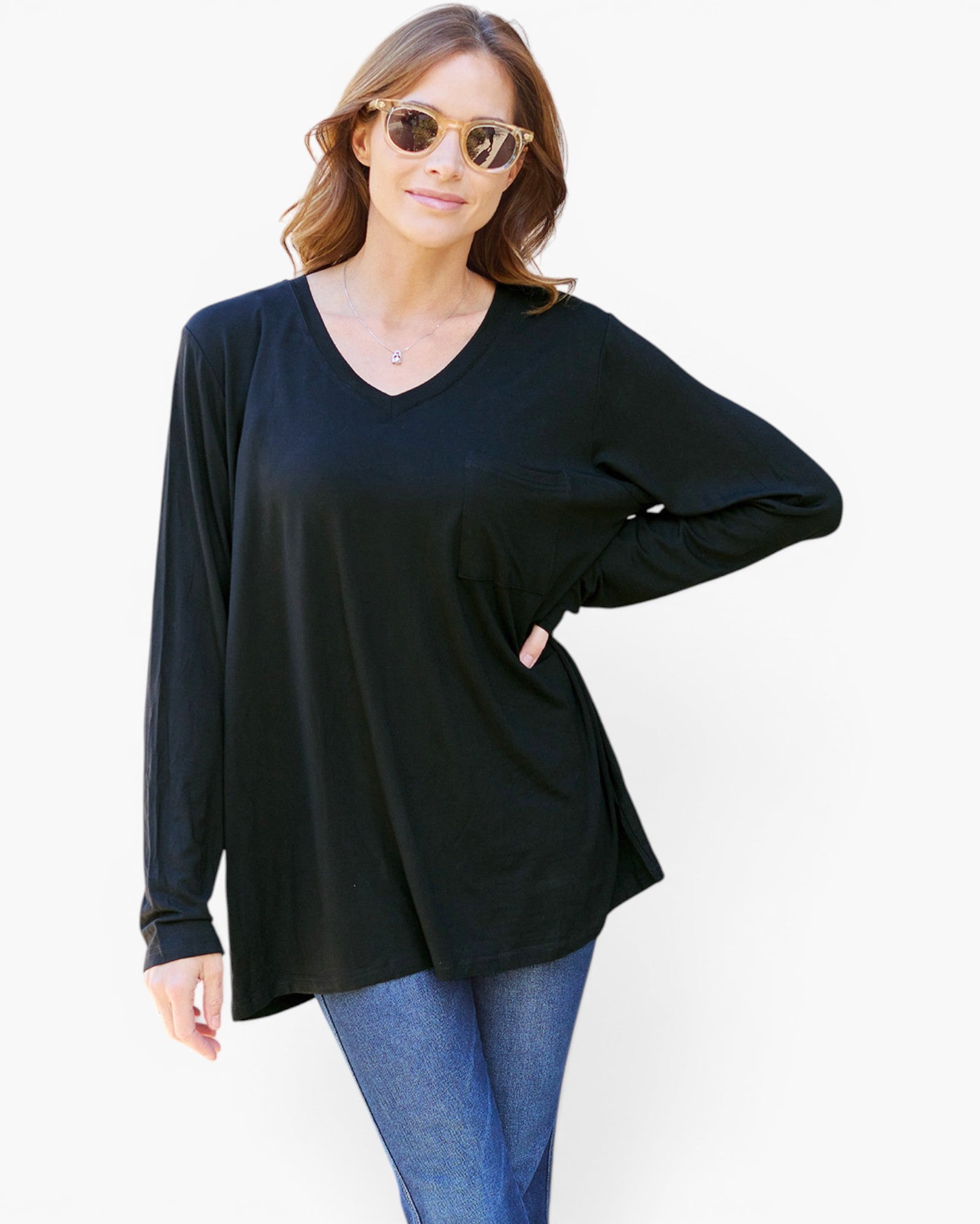 A woman modeling a black long-sleeve V-neck tunic top with blue jeans against a plain white background.