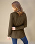 Woman wearing a brown long-sleeve top and blue jeans against a beige background