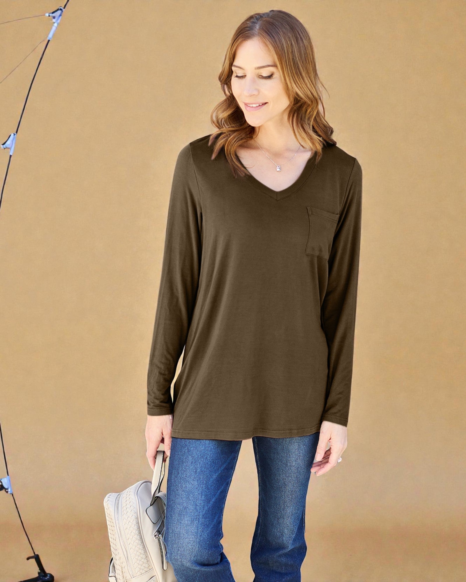 Woman wearing an olive green long-sleeve top and blue jeans against a beige background