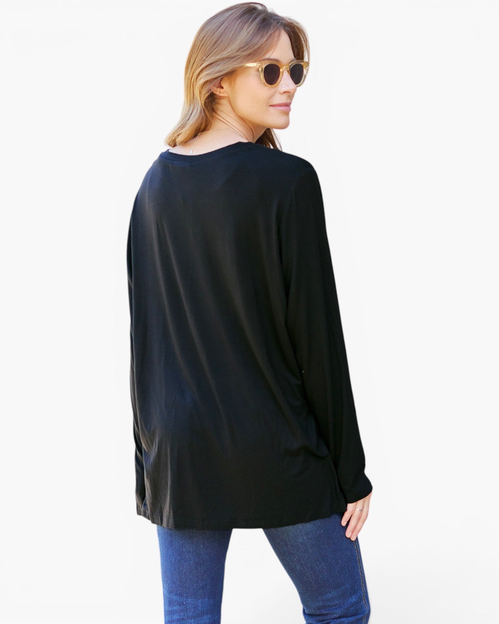 A woman wearing a loose black long-sleeve top and blue jeans, photographed from the back against a plain white studio background.