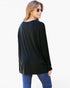 A woman wearing a loose black long-sleeve top and blue jeans, photographed from the back against a plain white studio background.