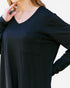 A close-up of a woman wearing a black long-sleeve V-neck top with a chest pocket, shown against a plain light background.