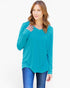 A woman modeling a teal long-sleeve V-neck top with blue jeans against a plain white background.
