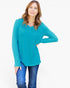 A woman modeling a teal long-sleeve scoop-neck top with blue jeans against a plain white studio background.