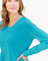 A woman wearing a bright turquoise long-sleeve V-neck top with a chest pocket, shown against a plain white background.