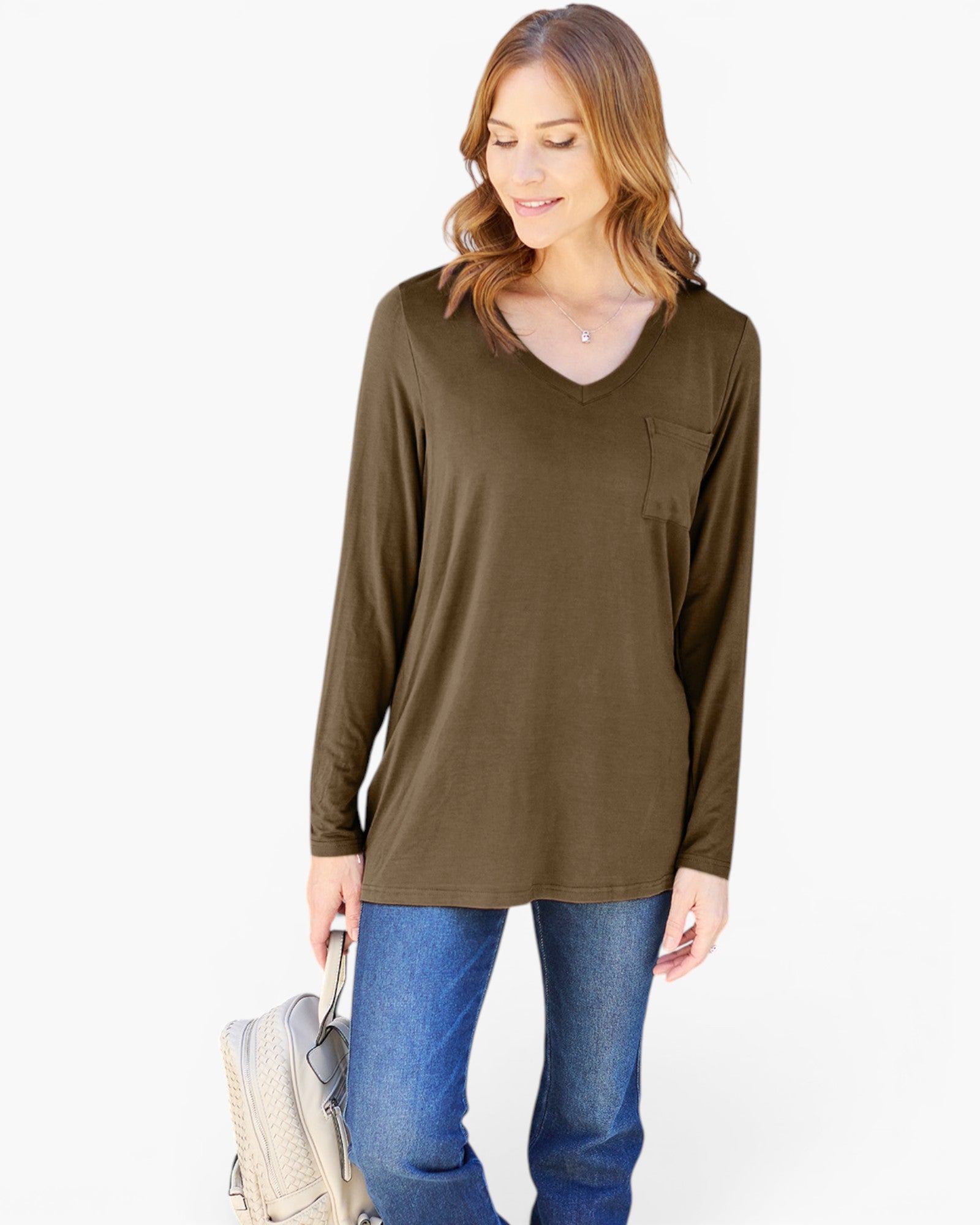 A woman wearing a long-sleeve V-neck tunic top in olive brown, paired with blue jeans, holding a light-colored shoulder bag against a plain white background.