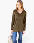 A woman wearing a long-sleeve V-neck tunic top in olive brown, paired with blue jeans, holding a light-colored shoulder bag against a plain white background.