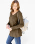 A woman wearing a long-sleeve V-neck olive green top and blue jeans, carrying a white woven backpack, photographed against a plain white background.