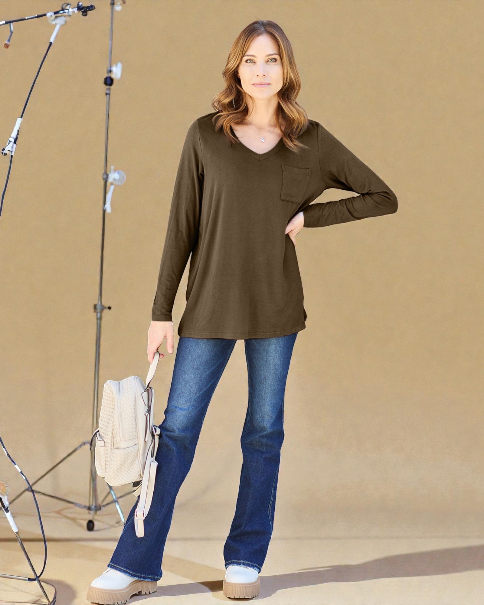 Woman wearing a brown long-sleeve top and blue jeans standing in front of studio equipment.