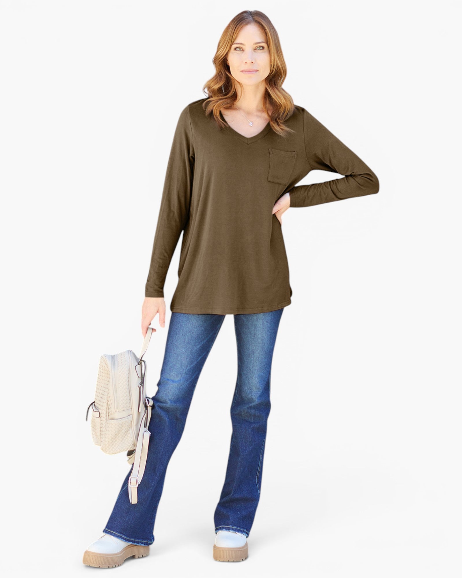A woman modeling a long-sleeve olive green V-neck top with a chest pocket, paired with blue jeans and holding a light beige backpack, against a plain white background.