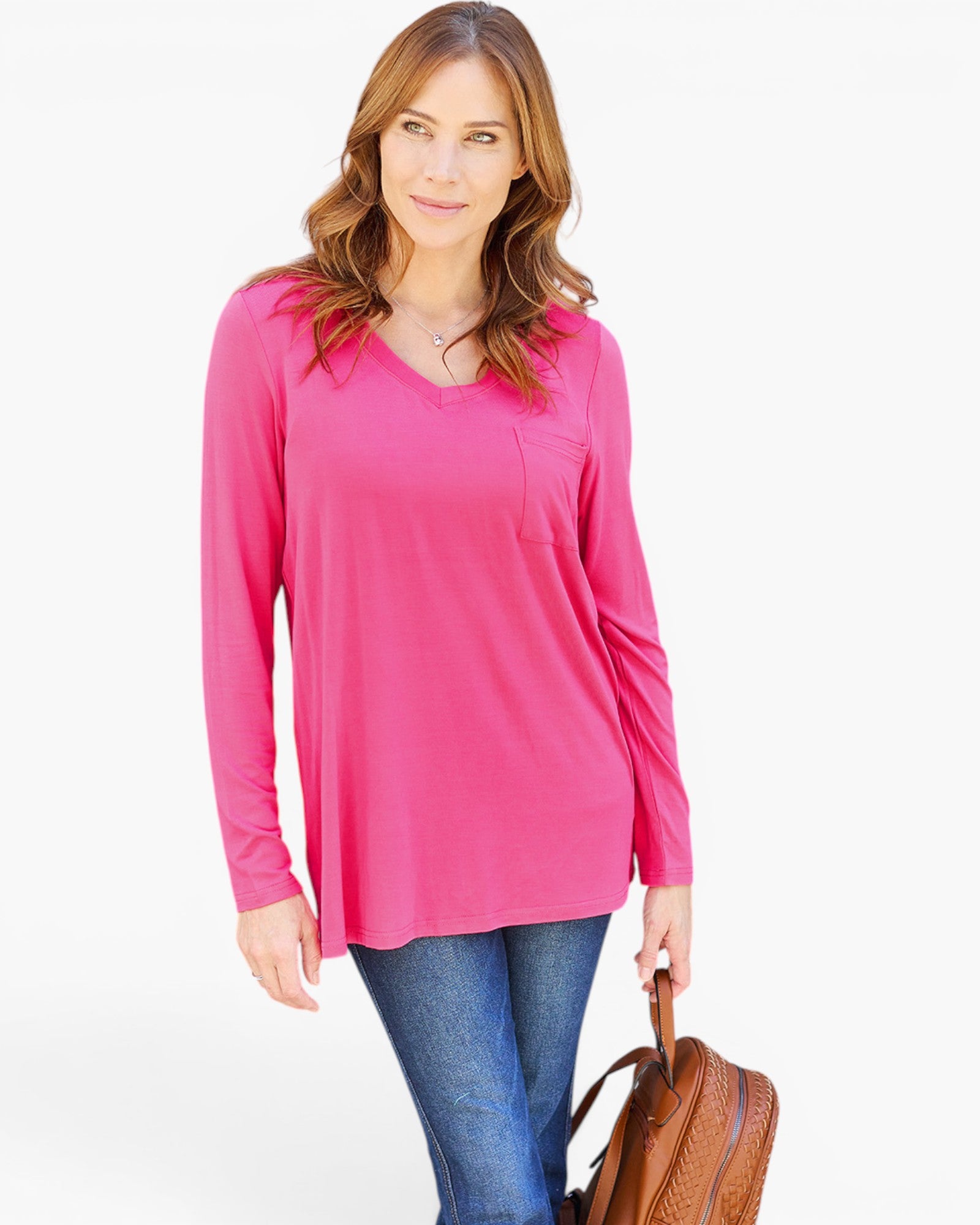 A woman modeling a bright pink long-sleeve V-neck top with a chest pocket, paired with blue jeans and holding a brown leather bag, against a plain white background.