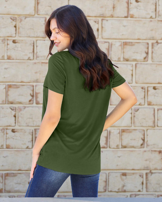 Woman wearing a green t-shirt and blue jeans standing against a brick wall.