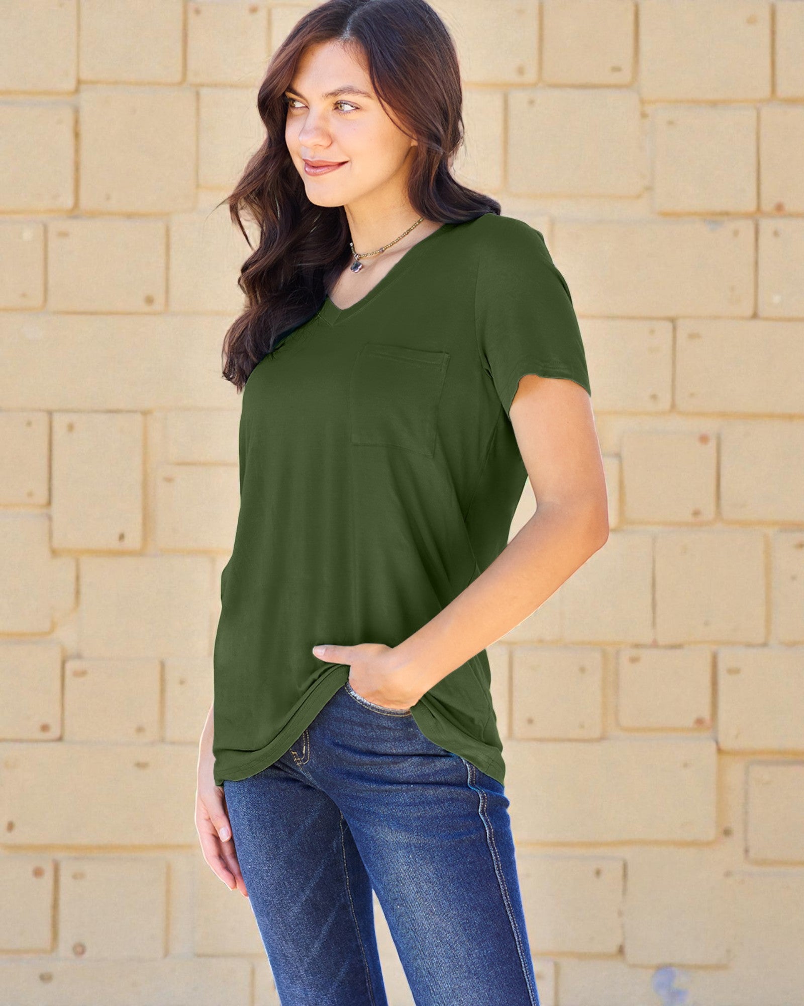 Woman wearing a green shirt and blue jeans against a beige brick wall