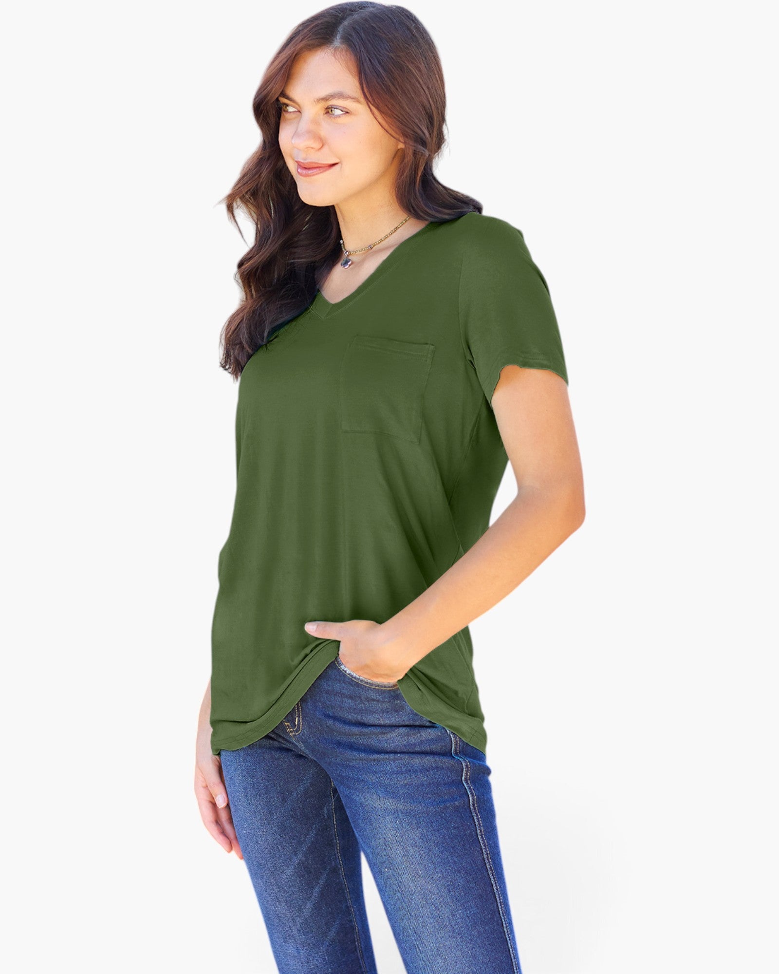 A woman wearing an olive green short-sleeve V-neck top with a chest pocket, paired with blue jeans, photographed against a plain white studio background.