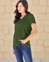 Woman wearing a green shirt and blue jeans against a beige brick wall