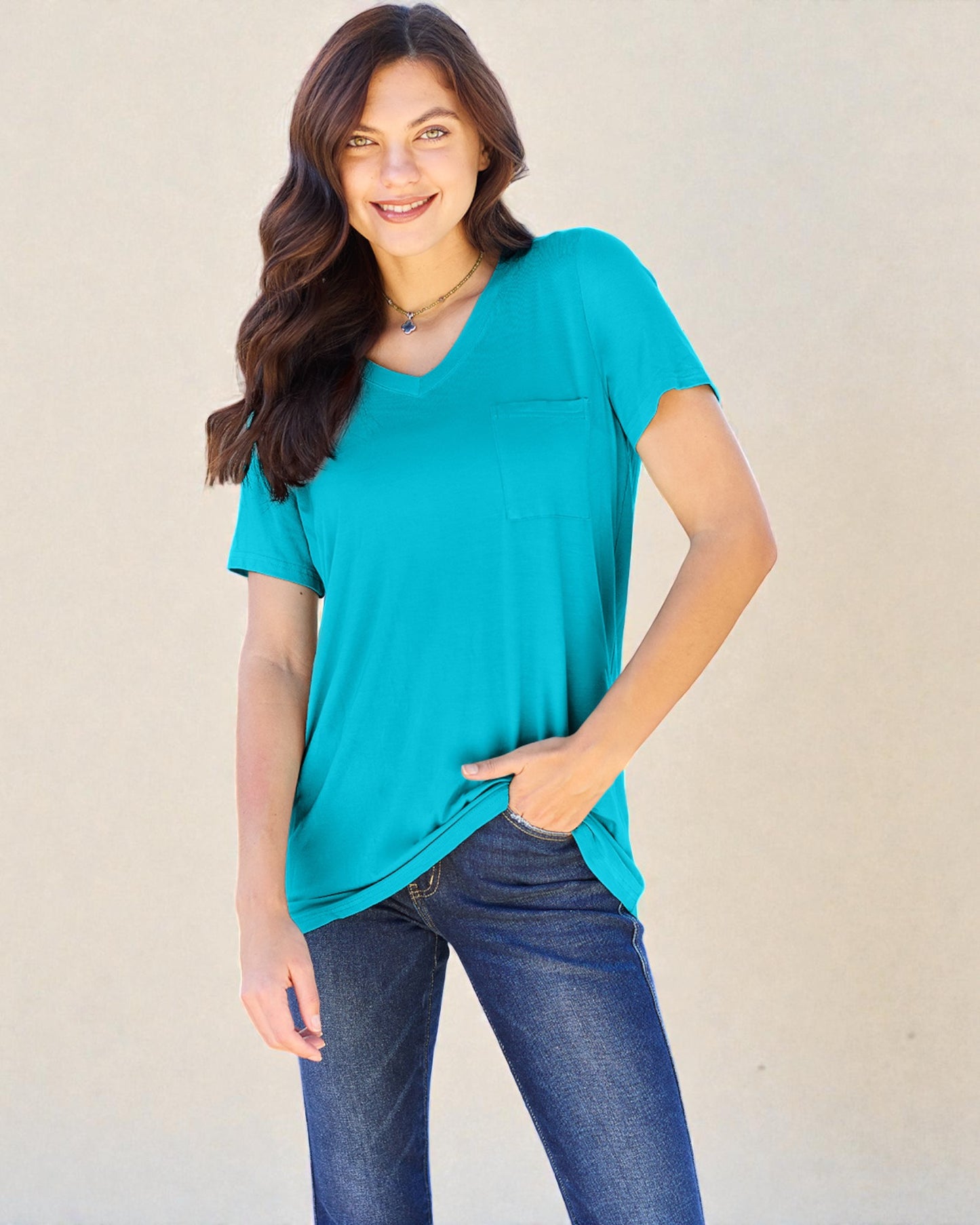 Woman wearing a teal t-shirt and blue jeans against a beige background