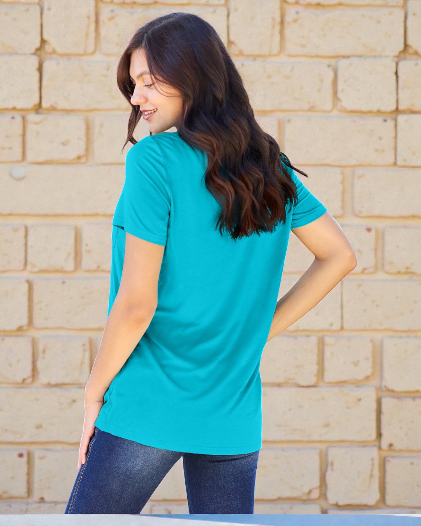 Woman wearing a turquoise shirt standing against a beige brick wall