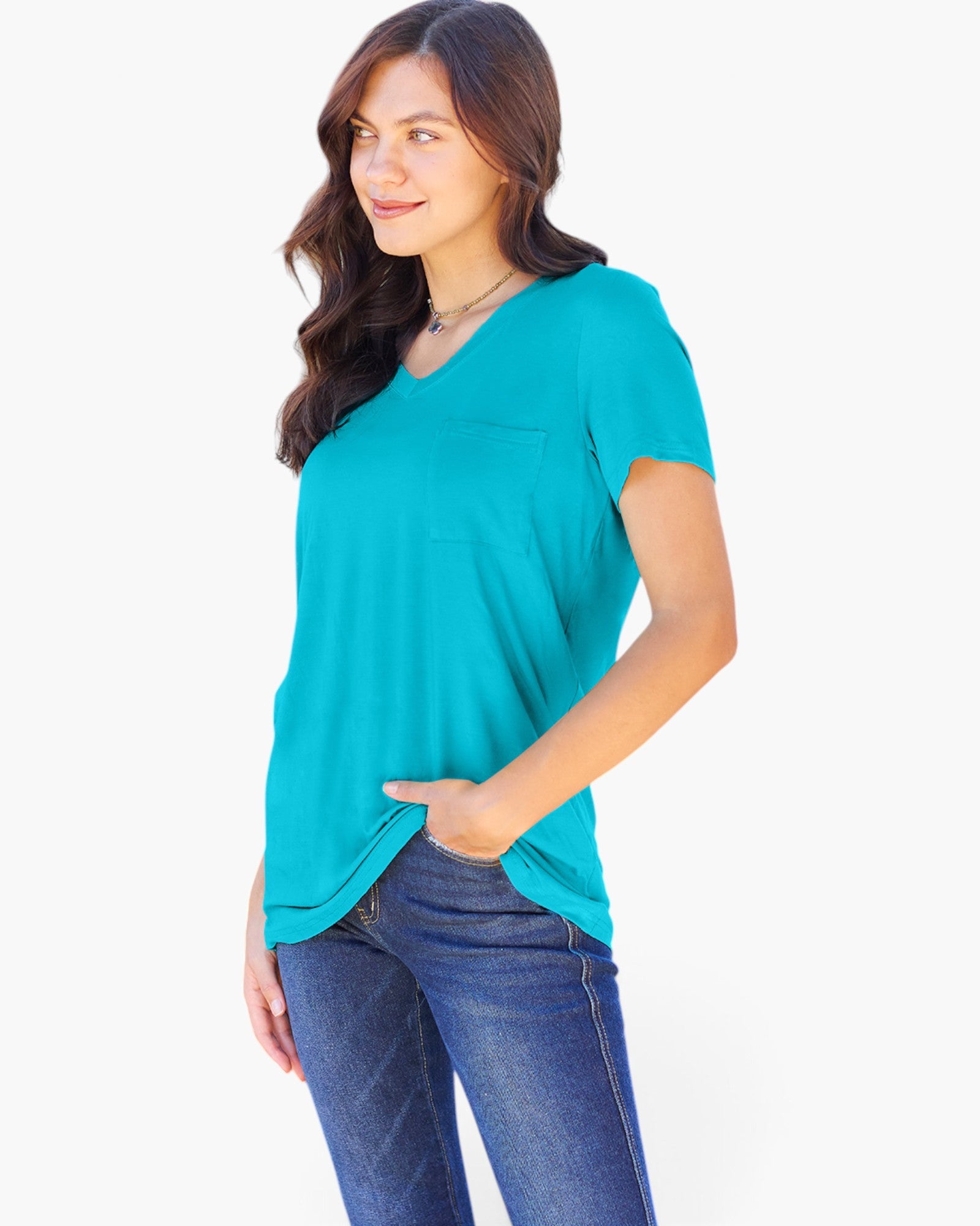 A woman wearing a bright turquoise short-sleeve V-neck top with a chest pocket and blue jeans, standing against a plain white studio background.