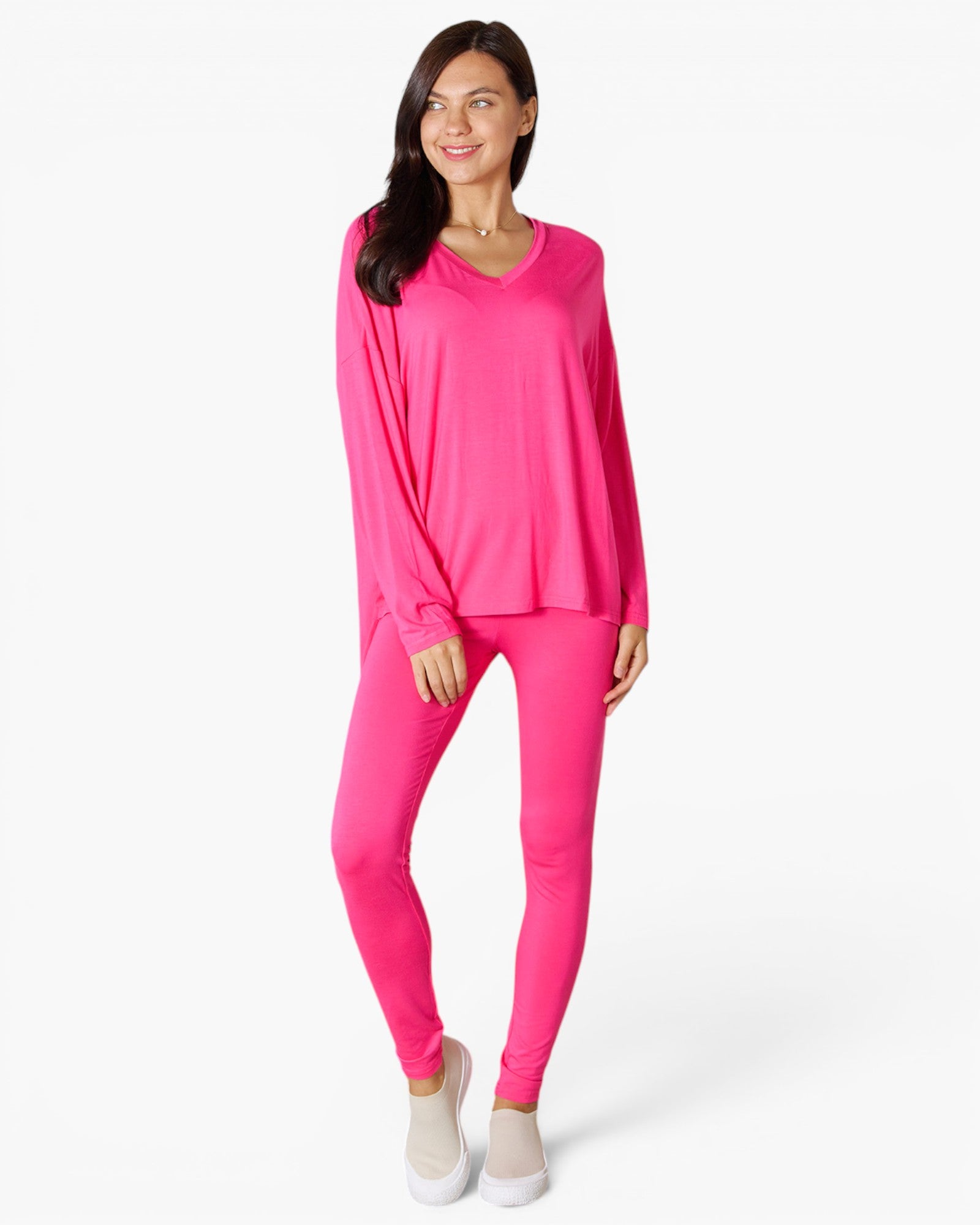 A woman modeling a bright pink matching lounge set consisting of a long-sleeve V-neck top and high-waisted leggings, paired with light beige slip-on shoes, against a plain white studio background.