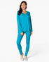 A woman modeling a matching two-piece loungewear set in a bright turquoise blue, featuring a long-sleeve V-neck top and high-waisted leggings, paired with light beige slip-on shoes against a plain white studio background.
