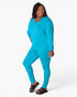 A woman modeling a matching turquoise blue lounge set consisting of a long-sleeve V-neck top and leggings, paired with black slide sandals, against a plain white studio background.