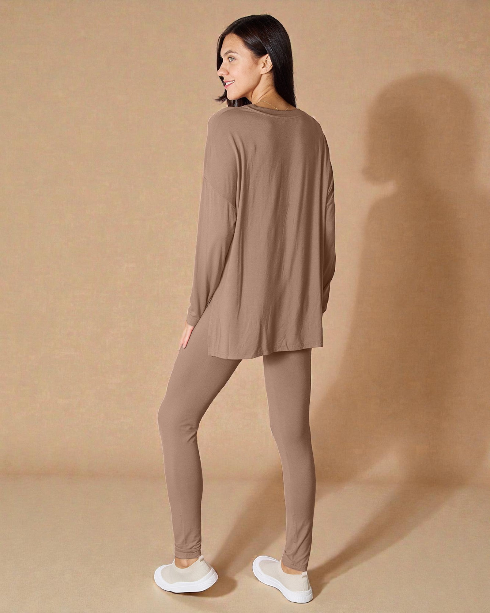 Woman wearing a brown long-sleeve top and leggings against a beige background