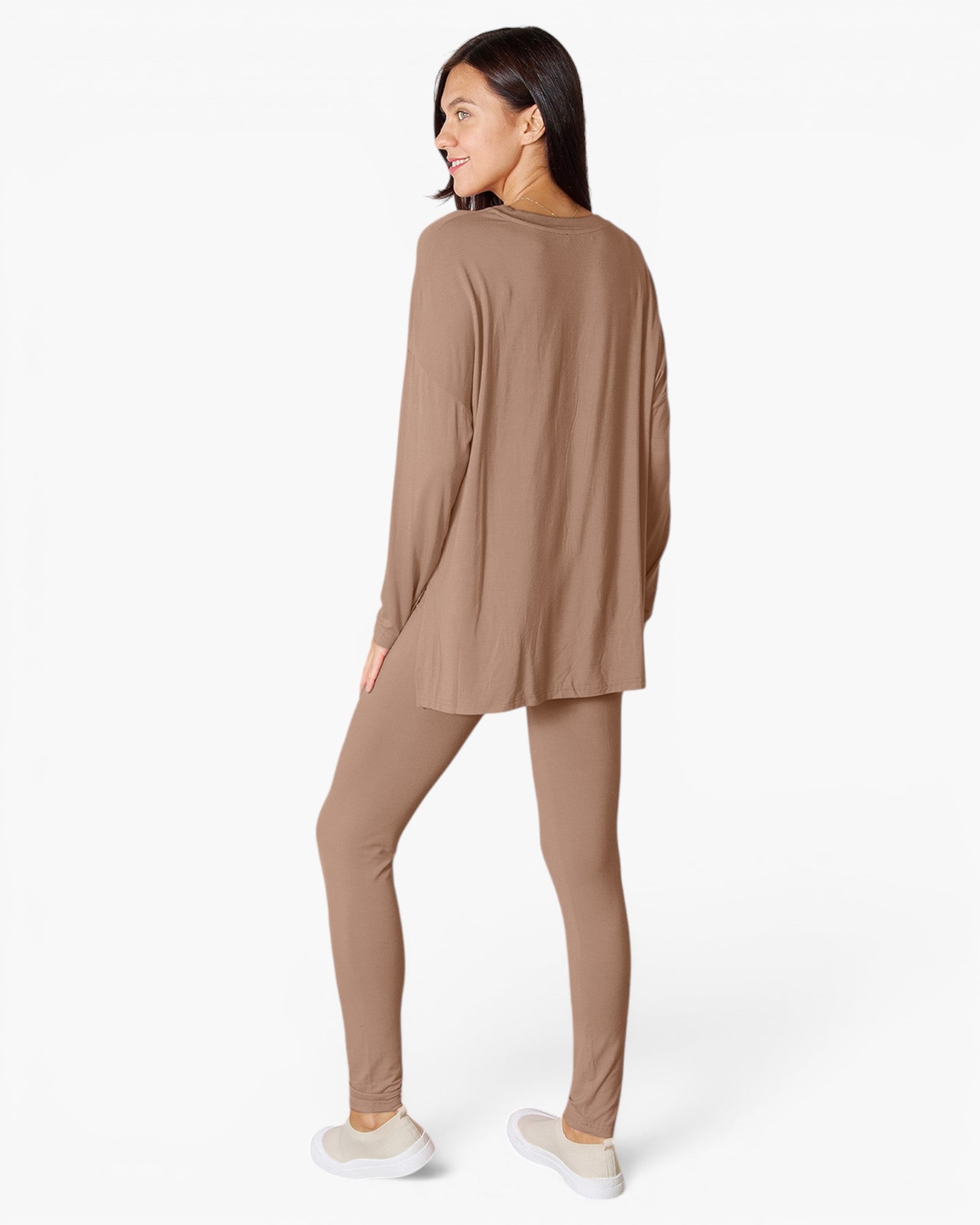 A woman wearing a matching two-piece lounge set in a warm taupe-brown color, featuring a long-sleeve tunic top and leggings, shown from a three-quarters back view against a plain white studio background.