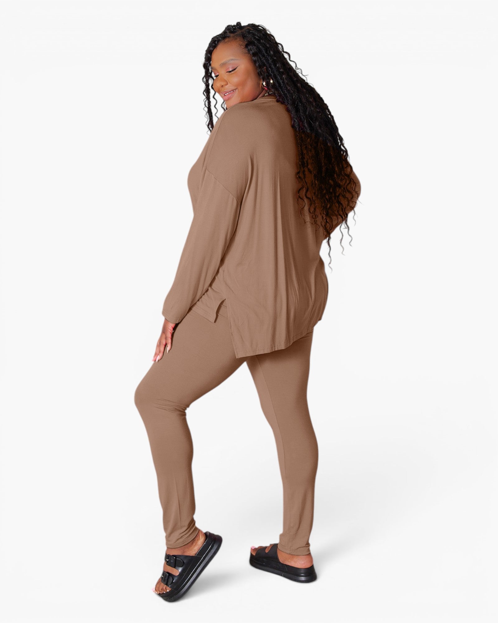 A woman modeling a matching two-piece lounge set in a warm taupe-brown color, featuring a long-sleeve top and leggings, against a plain white studio background.