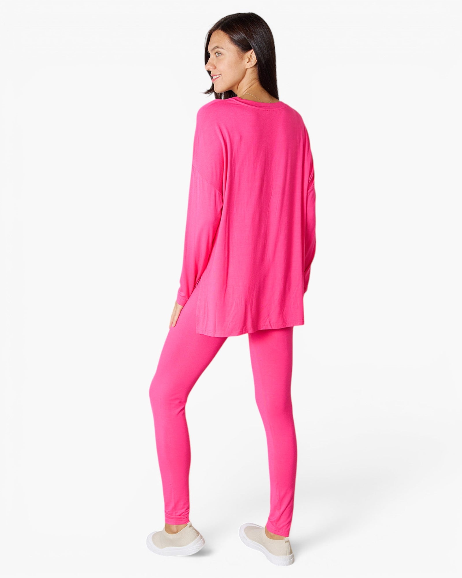 A woman wearing a bright pink lounge set consisting of a long-sleeve top and matching leggings, shown from a rear three-quarter angle against a plain white studio background.