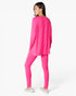 A woman wearing a bright pink lounge set consisting of a long-sleeve top and matching leggings, shown from a rear three-quarter angle against a plain white studio background.