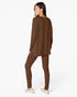 A woman modeling a matching brown lounge set consisting of a long-sleeve top and leggings, shown from a three-quarters back view against a plain white studio background.