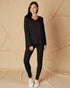 Woman wearing a black outfit standing against a beige background