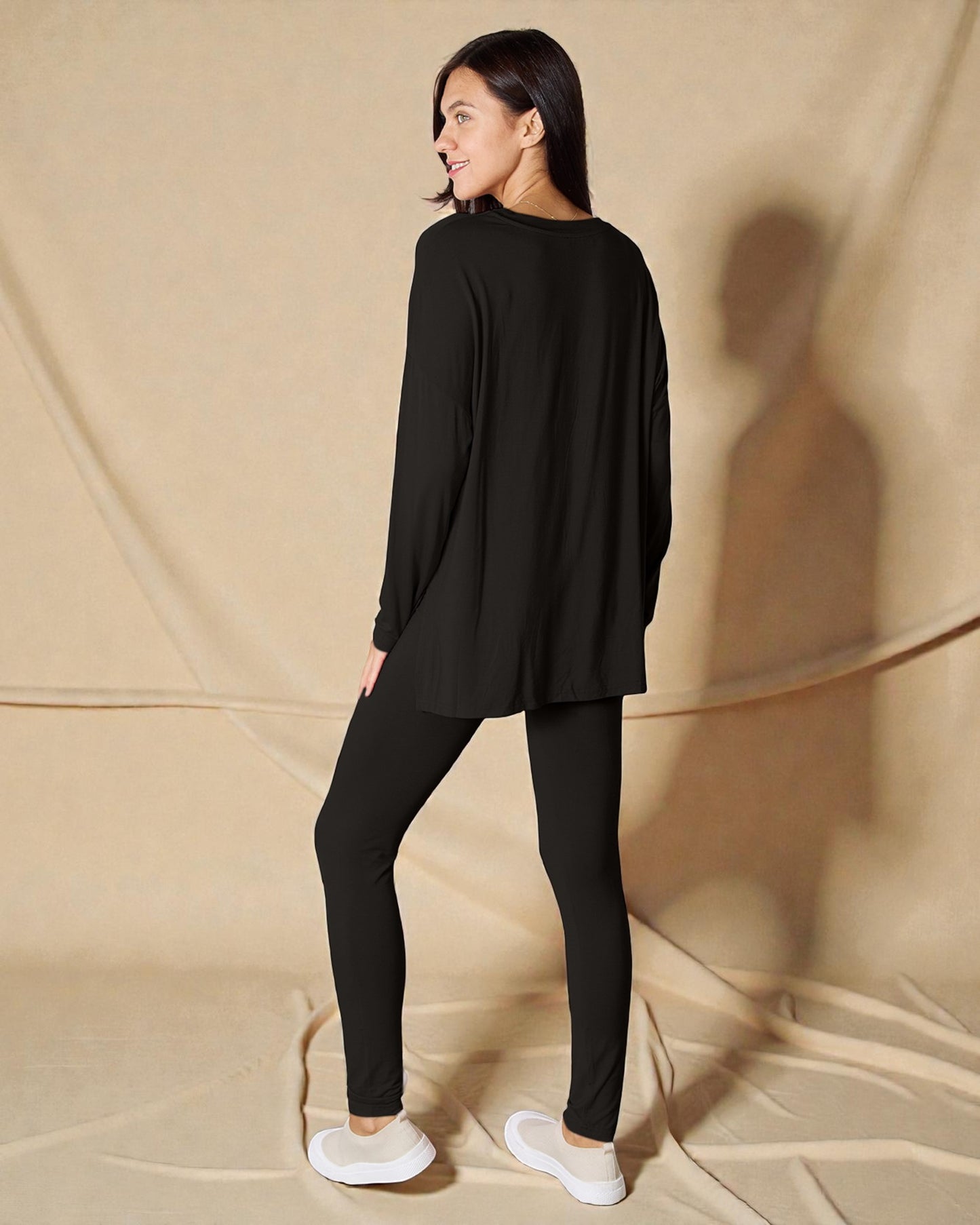 Woman wearing a black outfit standing against a beige background