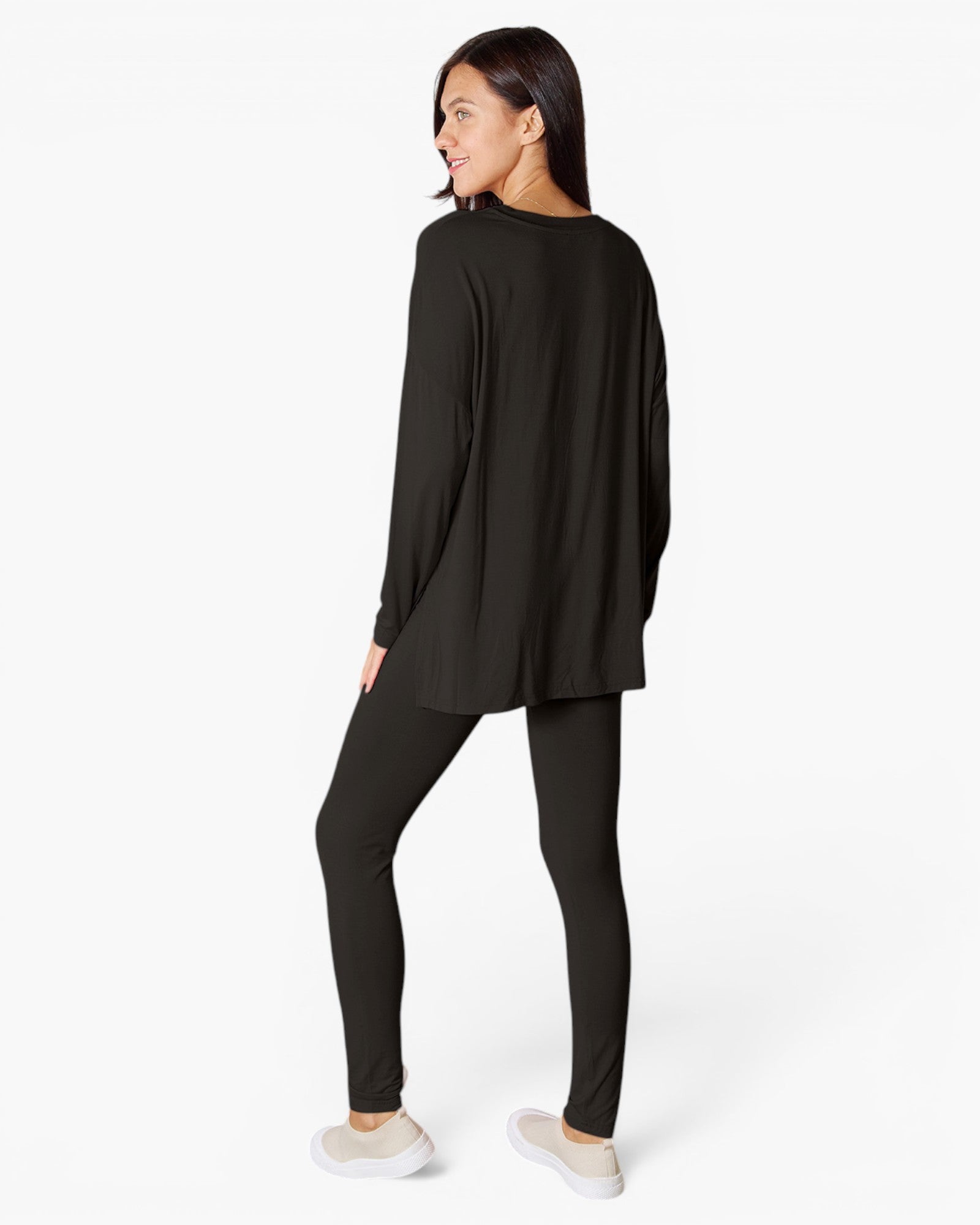 A woman modeling a black long-sleeve top and matching black leggings against a clean white studio background.