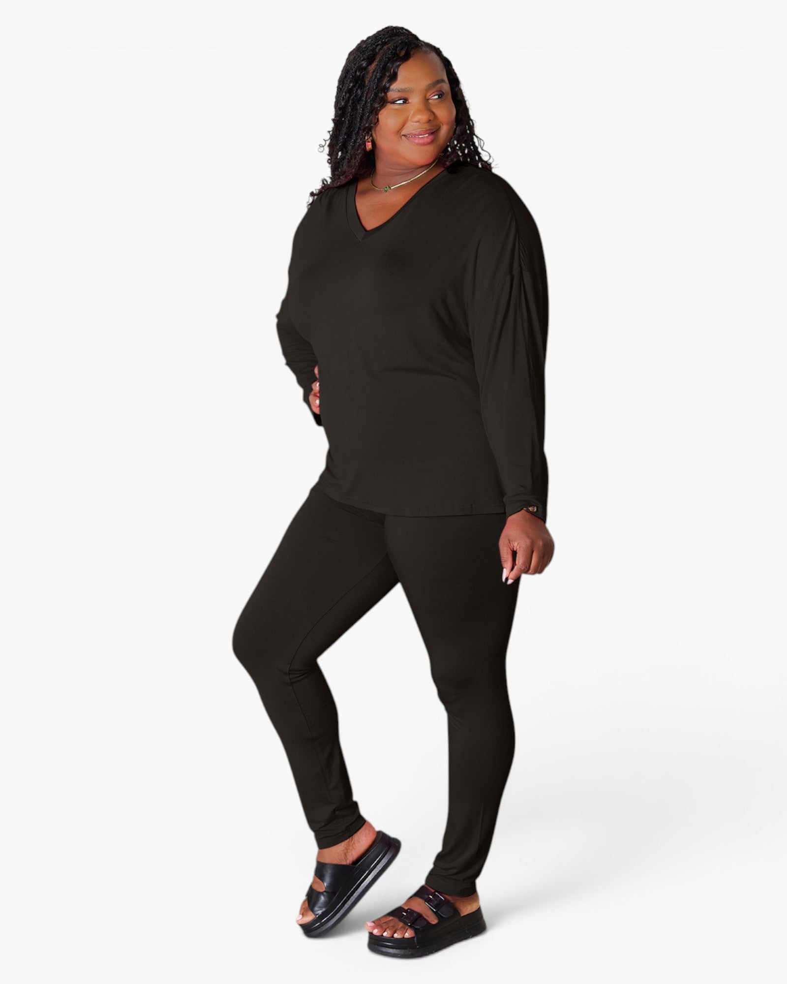 A woman modeling a black long-sleeve V-neck top and matching black leggings against a plain white studio background.