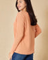 Woman wearing a peach-colored long-sleeve top against a beige background