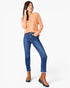 A woman modeling a peach long-sleeve henley top, blue skinny jeans, and brown ankle boots against a plain white studio background.