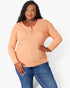 A woman modeling a peach-colored long-sleeve henley top with blue jeans against a plain white studio background.