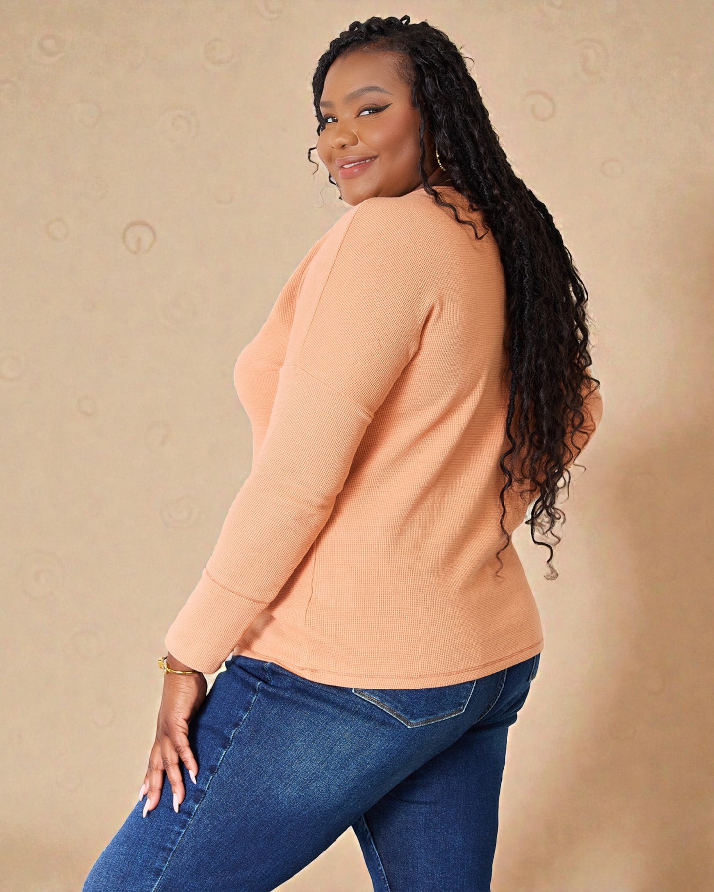 Woman wearing a peach sweater and blue jeans against a beige background