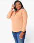 A woman modeling a peach-colored long-sleeve henley top with blue jeans against a plain white studio background.